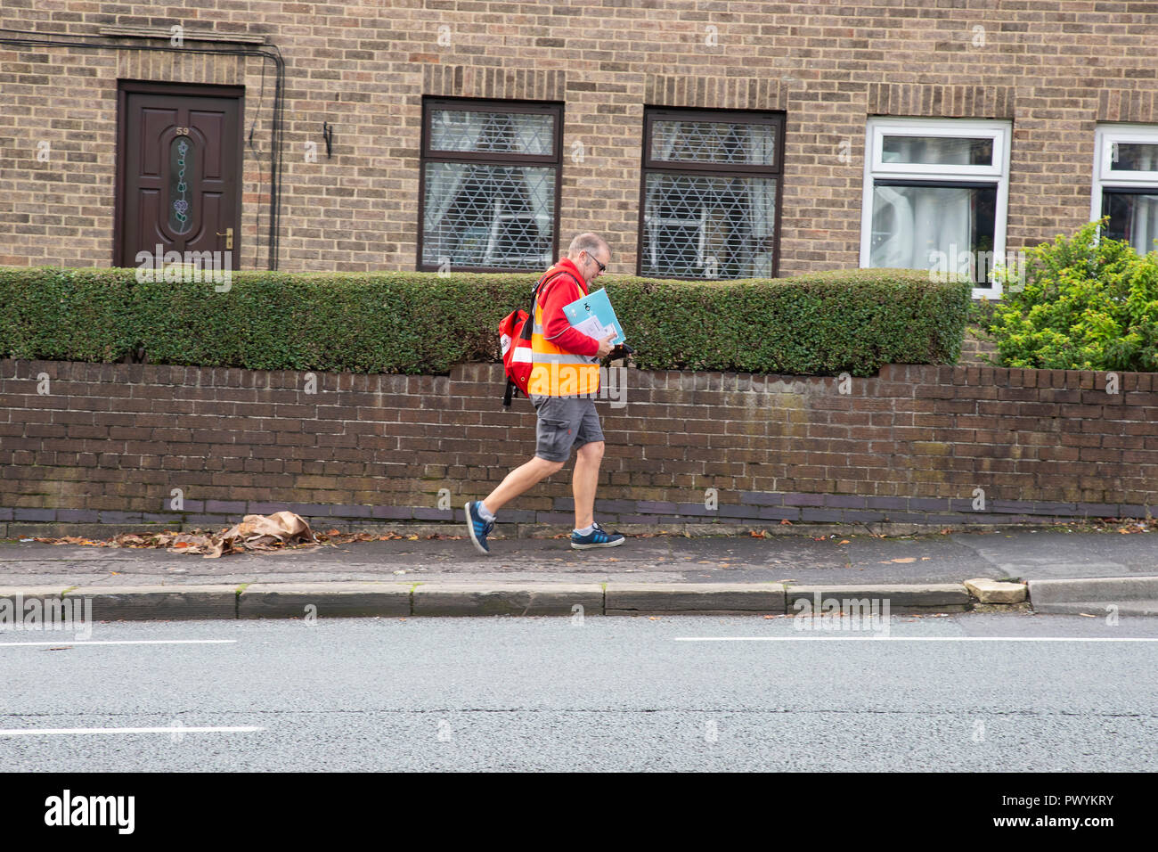 British postino consegna la posta a piedi sul suo tondo postale Foto Stock