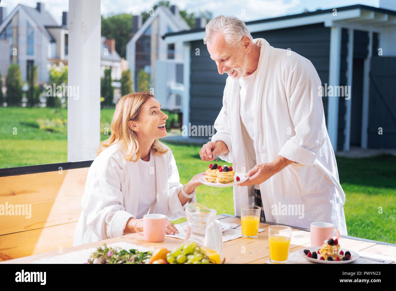 Amorevole marito maturo avendo cura di sua moglie che serve pancake con frutta per lei Foto Stock