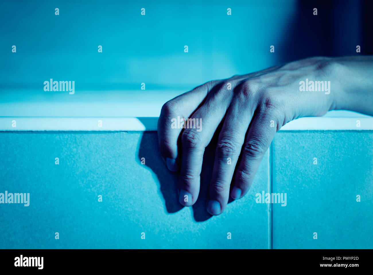 Primo piano della mano di un giovane uomo caucasico su di un lato della vasca, in un'atmosfera da brivido Foto Stock