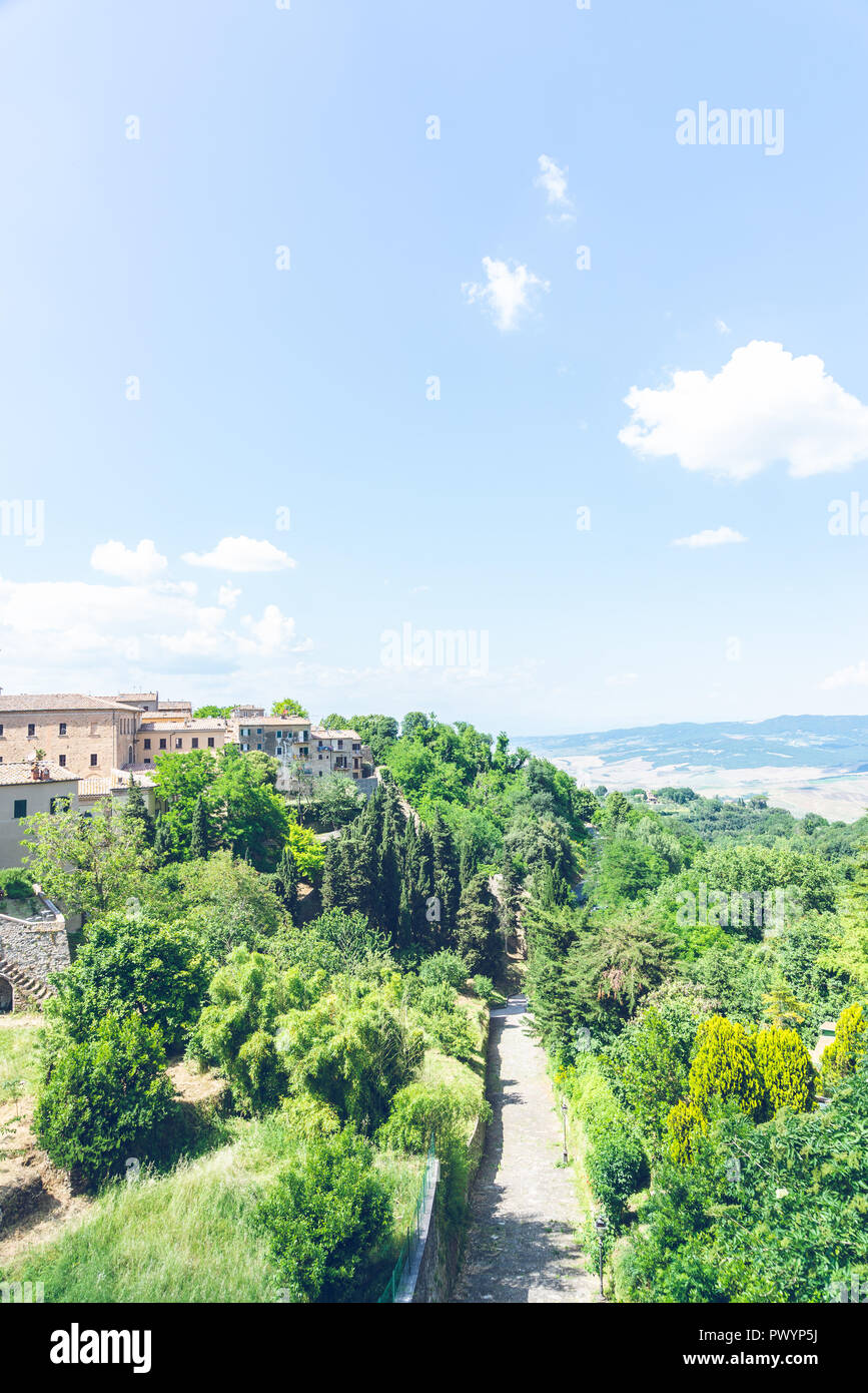 Foto verticale con strada vuota. La pista va tra diversi alberi verdi lungo l antica città volterà. La città è in Toscana - Italia. Il cielo è blu w Foto Stock