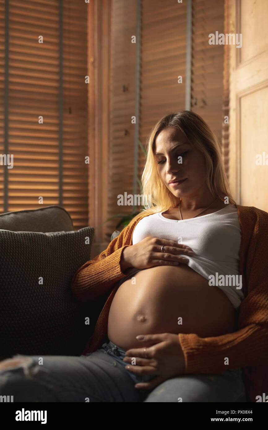 Donna incinta seduta sul divano di toccare la sua pancia Foto Stock