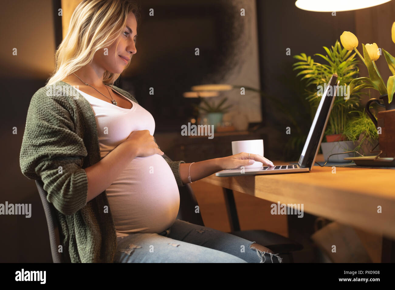 Donna incinta toccando il suo ventre e utilizzo di computer portatile Foto Stock