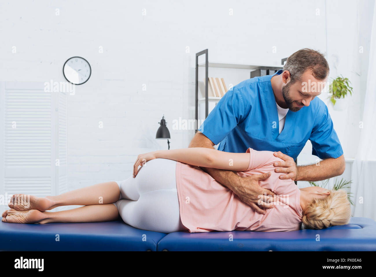 Sorridente massaggio chiropratico di schiena del paziente sdraiato sul lettino da massaggio in ospedale Foto Stock
