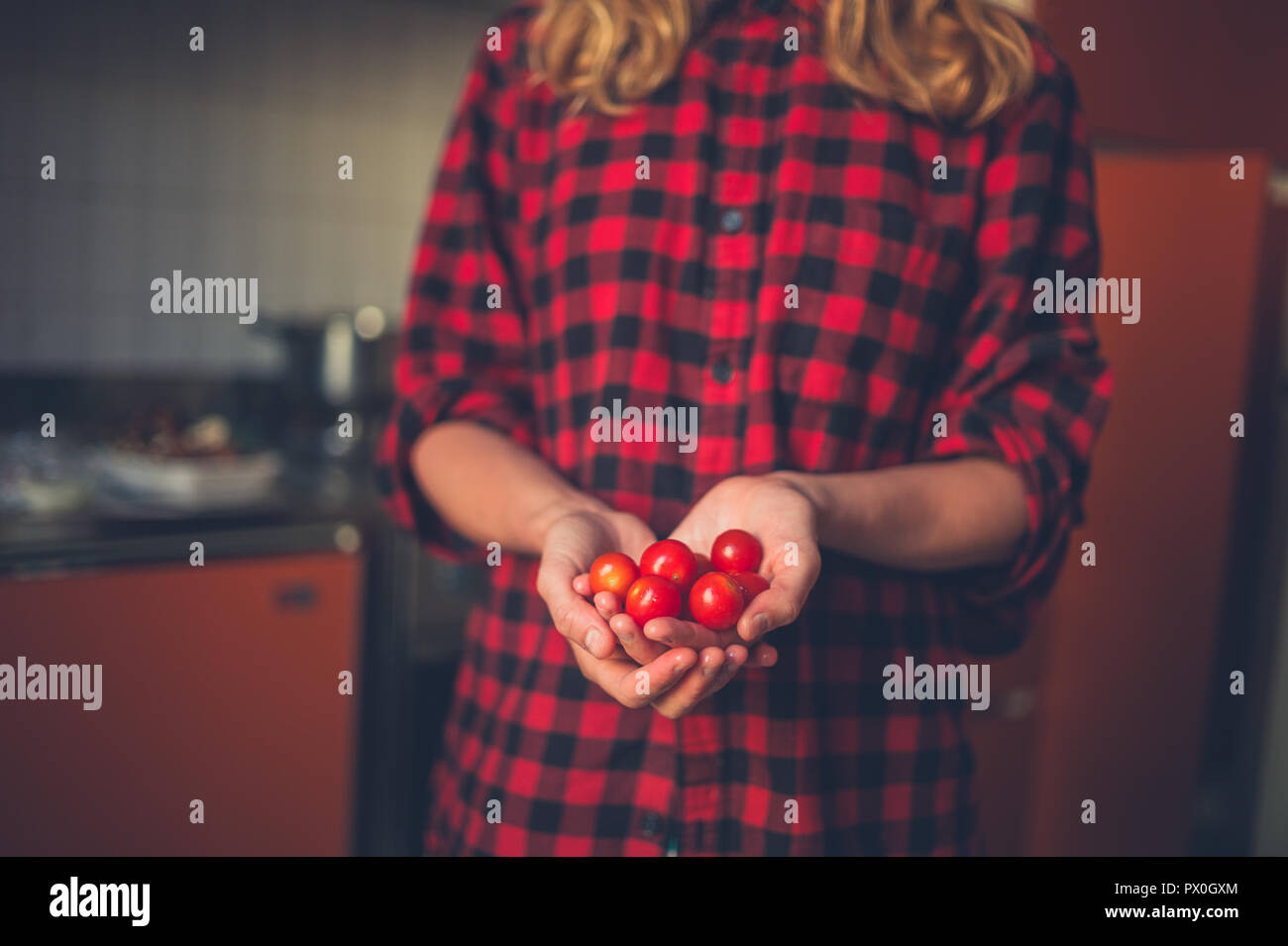 Una giovane donna è in piedi nella sua cucina con alcuni pomodori Foto Stock