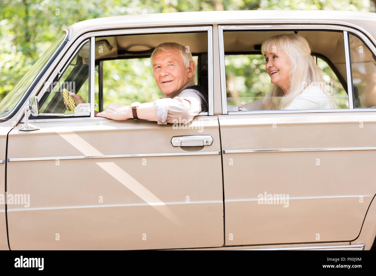 Vista laterale di sorridere coppia senior in seduta beige auto d'epoca Foto Stock