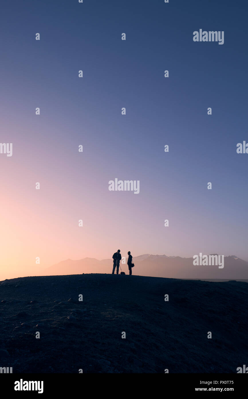 Le sagome dei fotografi turistici nel sole di mezzanotte e nel paesaggio islandese - fotografia di paesaggio Foto Stock