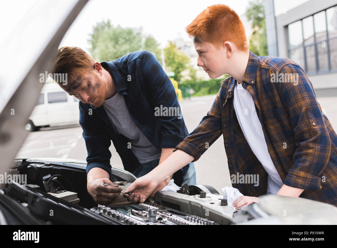 Figlio dando l'attrezzo per la riparazione di auto al padre Foto Stock