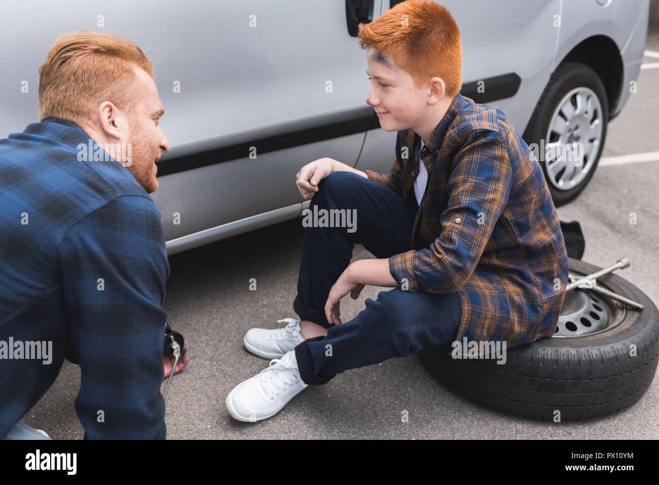 Padre e figlio cambiare pneumatico in auto con un martinetto e guardando ogni altro Foto Stock