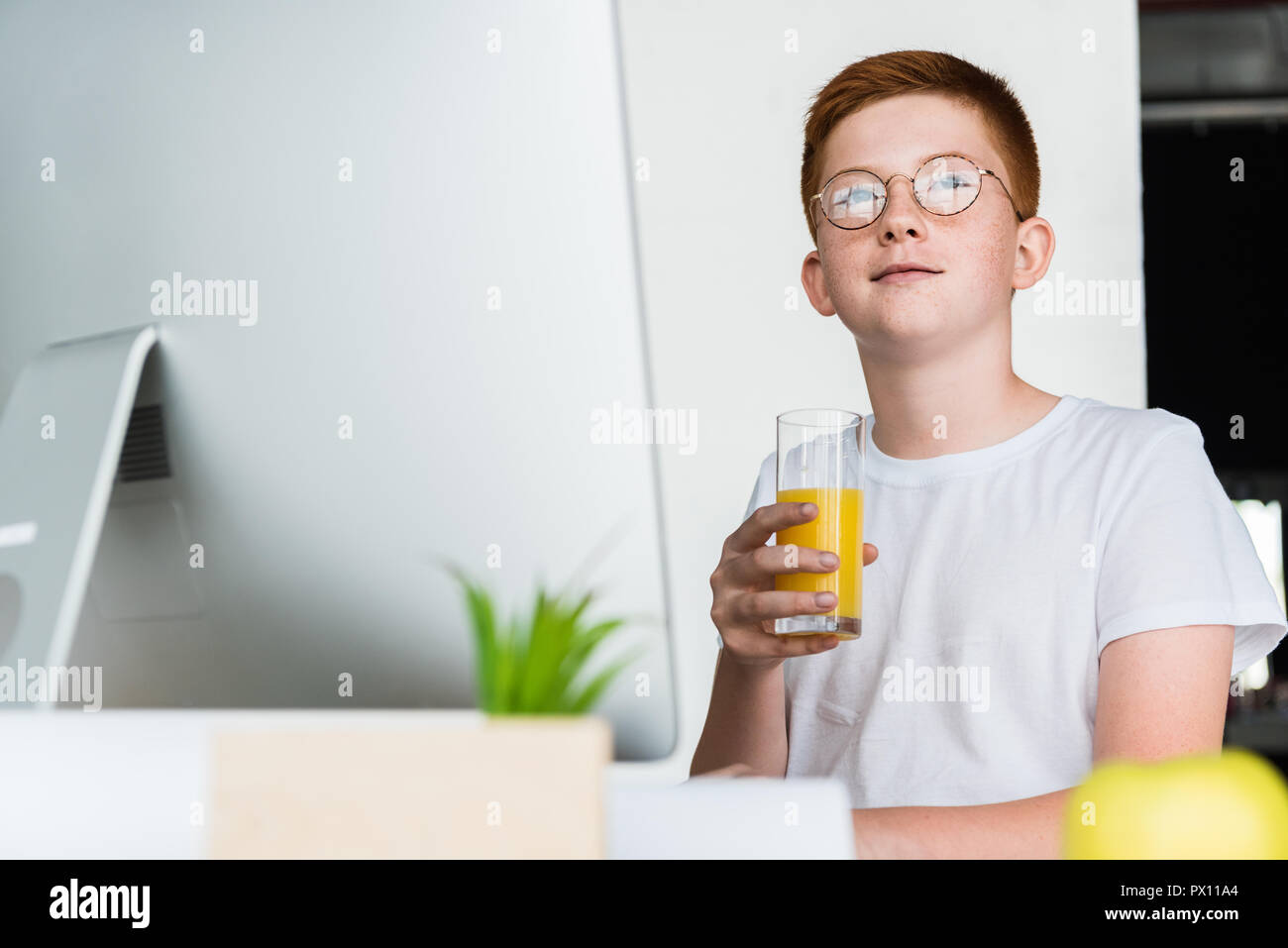 Lo zenzero preteen boy capelli tenendo un bicchiere di succo di frutta a casa Foto Stock