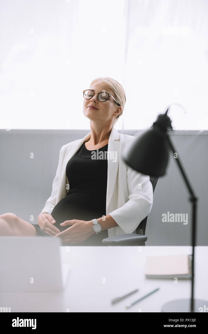 Ritratto di gravidanza imprenditrice in occhiali al lavoro in ufficio Foto Stock