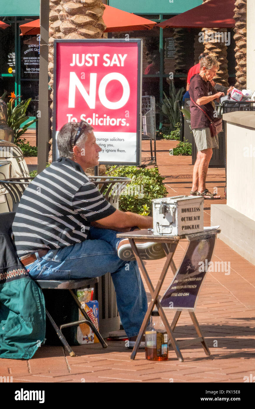 Ignaro di un segno che vieta gli avvocati a un Irvine, CA, shopping mall, un paziente volontario mans una cassetta di raccolta per i senzatetto. Foto Stock