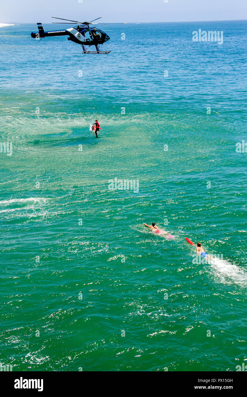Una città elicottero scende il personale di soccorso di bagnini in acqua per facilitare una vittima di annegamento in un oceano di salvataggio di sicurezza in Huntington Beach, CA. Foto Stock