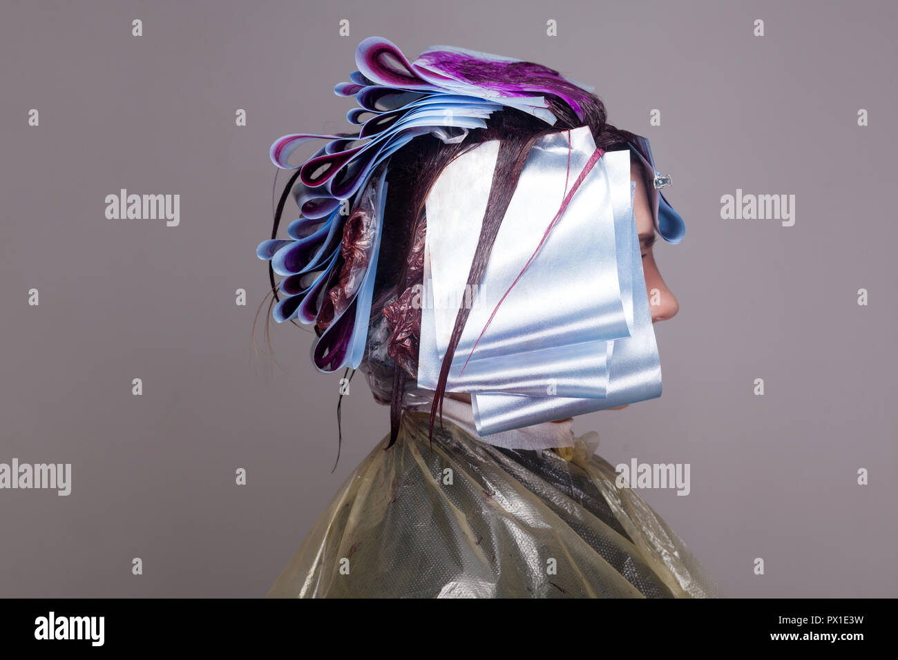 Profilo vista laterale della donna seduta e in attesa di un processo di tintura per capelli colorazione. piscina studio shot, isolata su uno sfondo grigio. Foto Stock