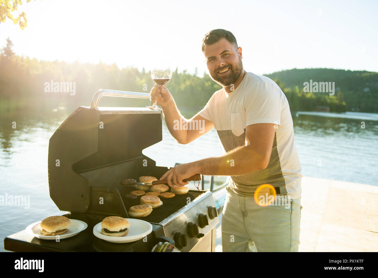 Padre Preparare hamburger su un grill all'aperto vicino ad un lago Foto Stock