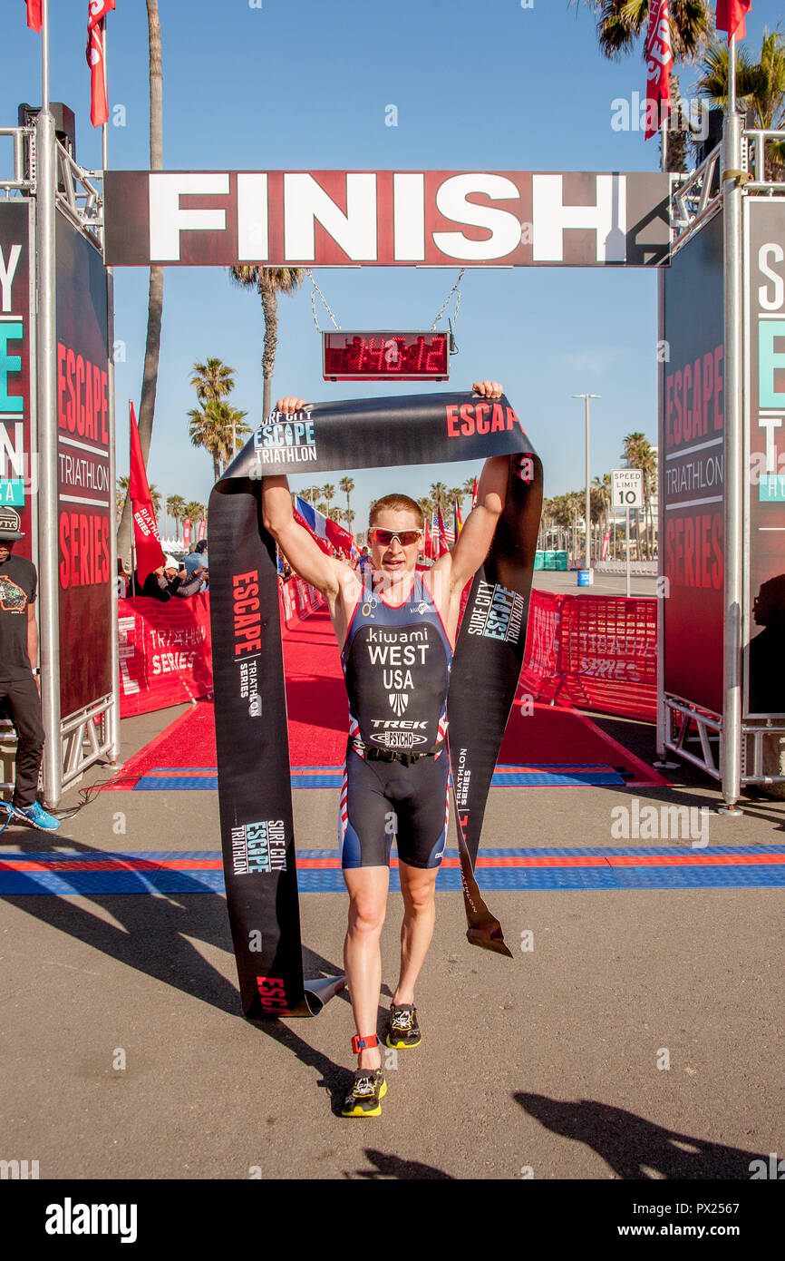Il vincitore di un triathlon via evento in Huntington Beach, CA, onde trionfalmente il traguardo a nastro. Foto Stock