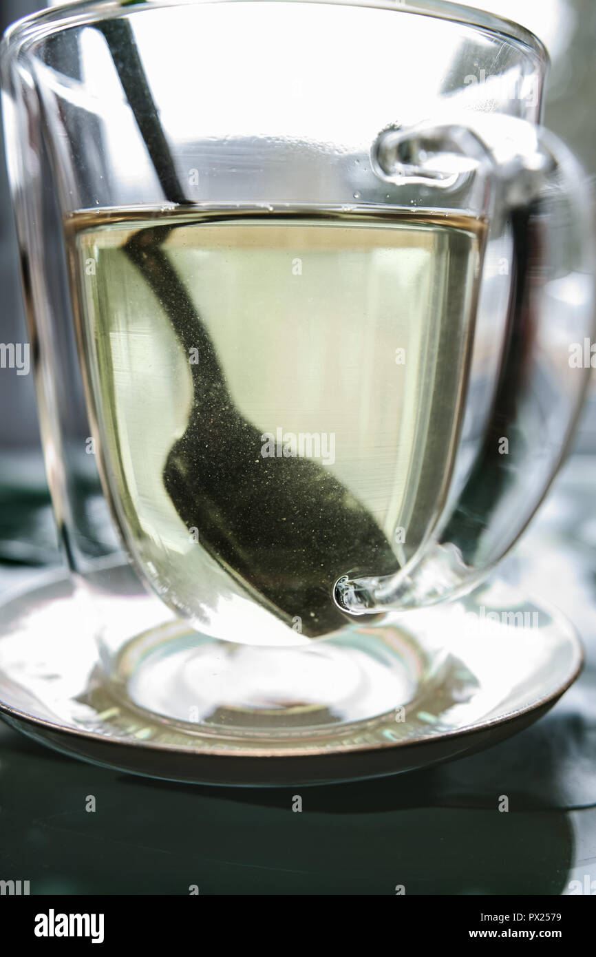 In un vetro trasparente tazza di tè bianco, vediamo un cucchiaino, in un effetto di ingrandimento. Foto Stock