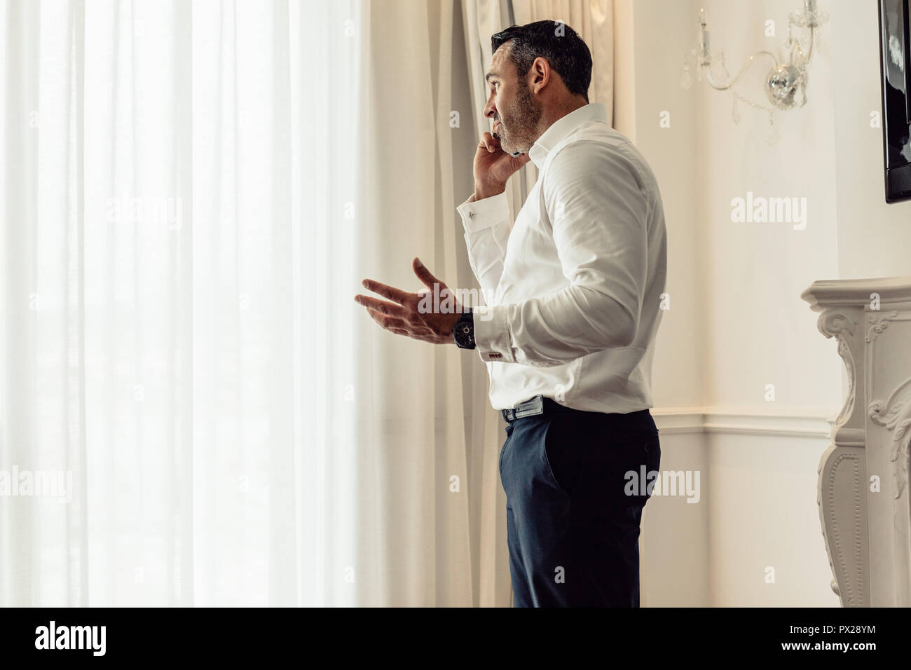 Vista laterale di imprenditore parlando al telefono cellulare mentre in piedi nella stanza dell'hotel. Amministratore Delegato avente un importante discutere al telefono. Foto Stock