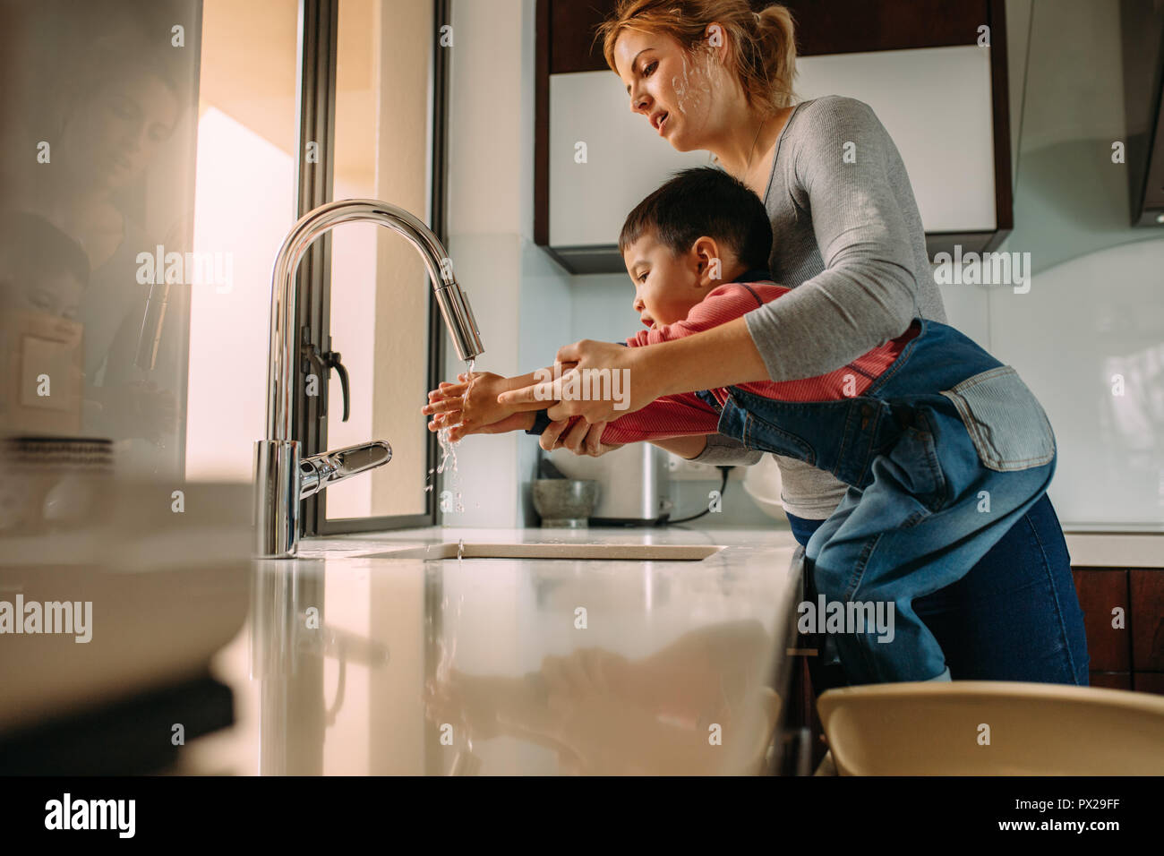 Carino figlio lavarsi le mani con la madre nel lavandino dopo la cottura. Donna aiutando ragazzino di lavare le mani al lavello. Foto Stock
