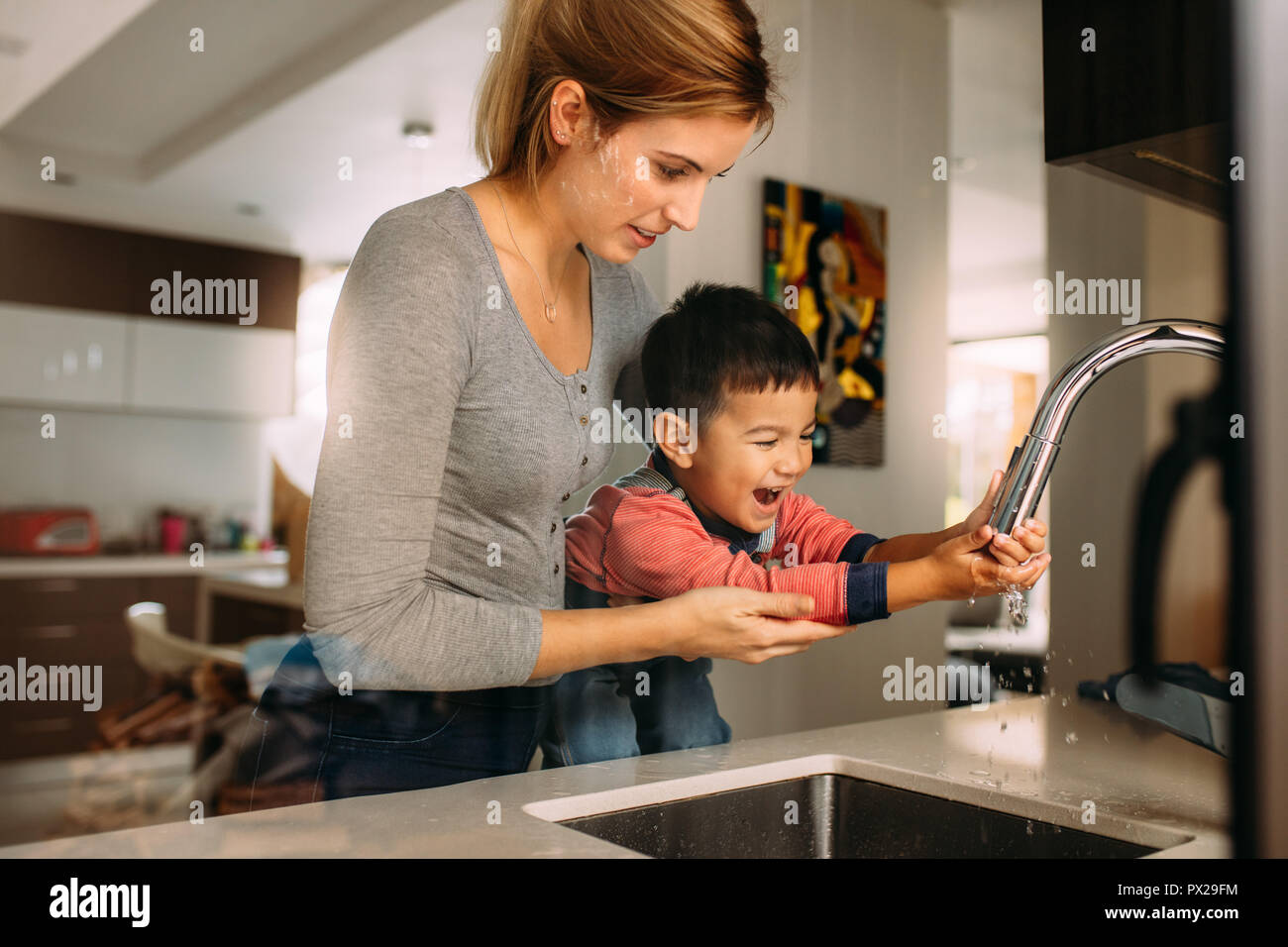 Carino figlio lavaggio delle mani con il sostegno di sua madre nel lavello. Donna aiutando ragazzino di lavarsi le mani dopo la cottura. Foto Stock