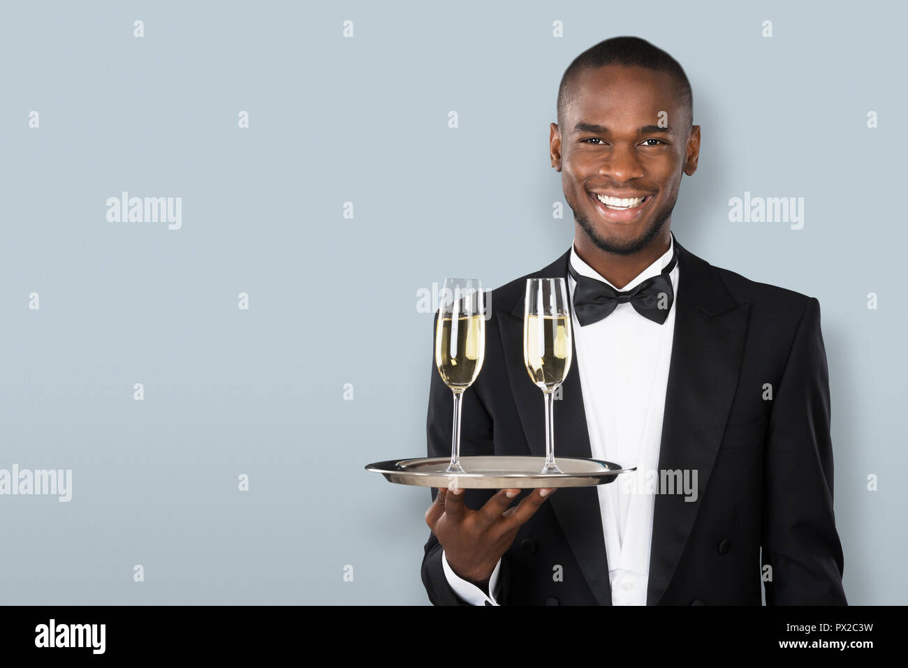 Ritratto di un sorridente cameriere africano Holding Champagne su sfondo grigio Foto Stock