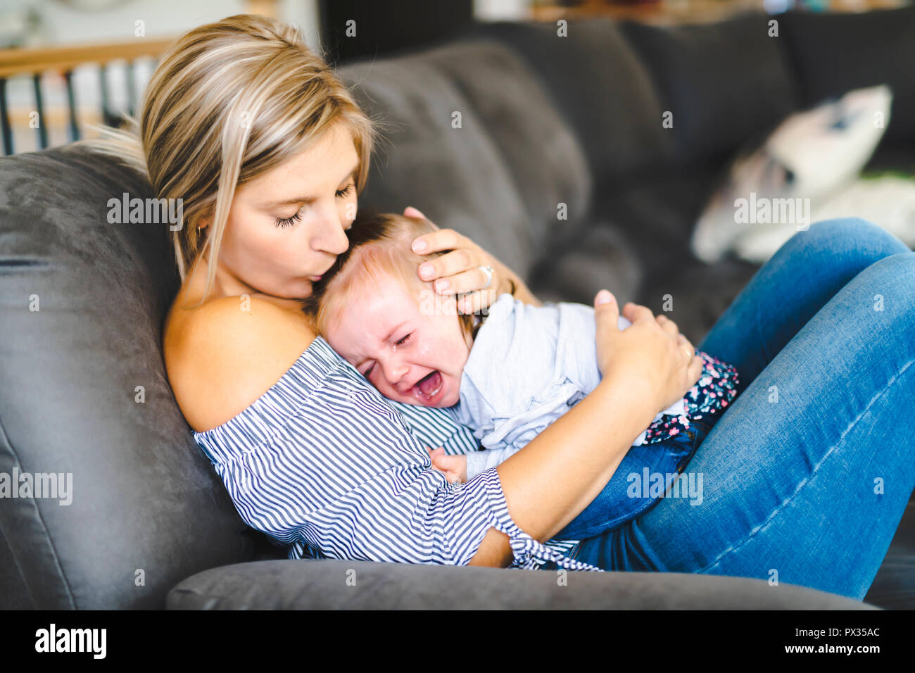 Giovane madre con bambino figlia sul divano di casa, il bambino piange Foto Stock