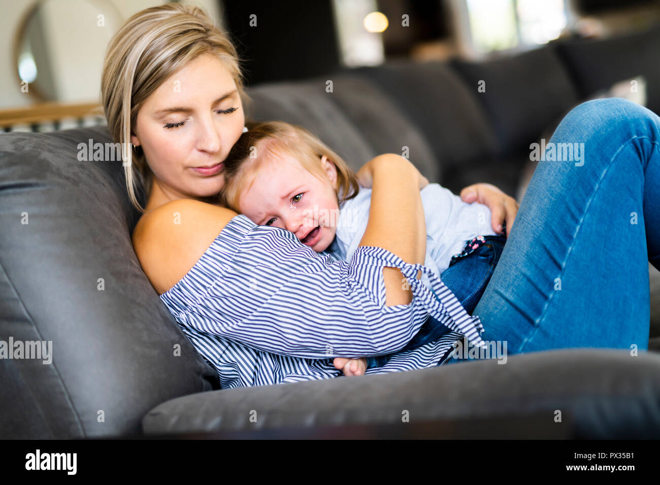 Giovane madre con bambino figlia sul divano di casa, il bambino piange Foto Stock