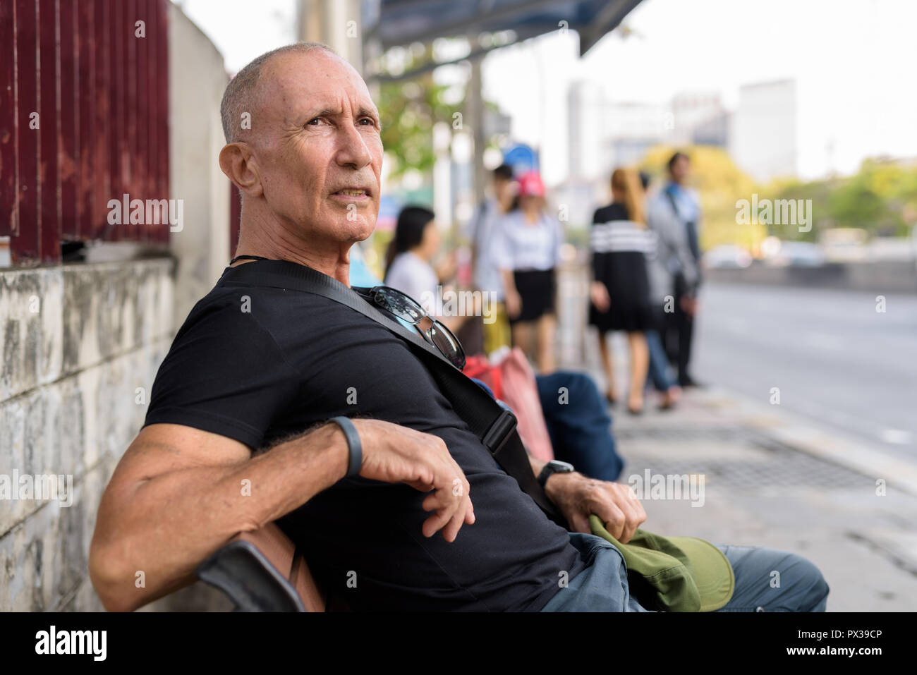 Bald senior uomo turistica in attesa e sedersi sul banco di legno a t Foto Stock