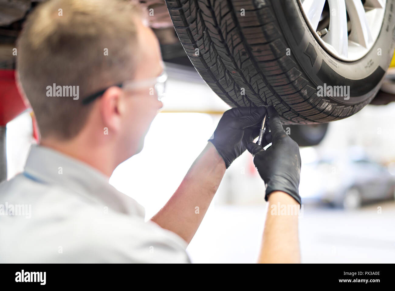 Bel lavoro meccanico in uniforme a lavorare sulla vettura controllare l'usura dei pneumatici Foto Stock