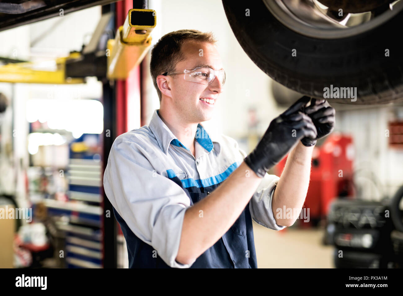 Bel lavoro meccanico in uniforme a lavorare sulla vettura controllare l'usura dei pneumatici Foto Stock