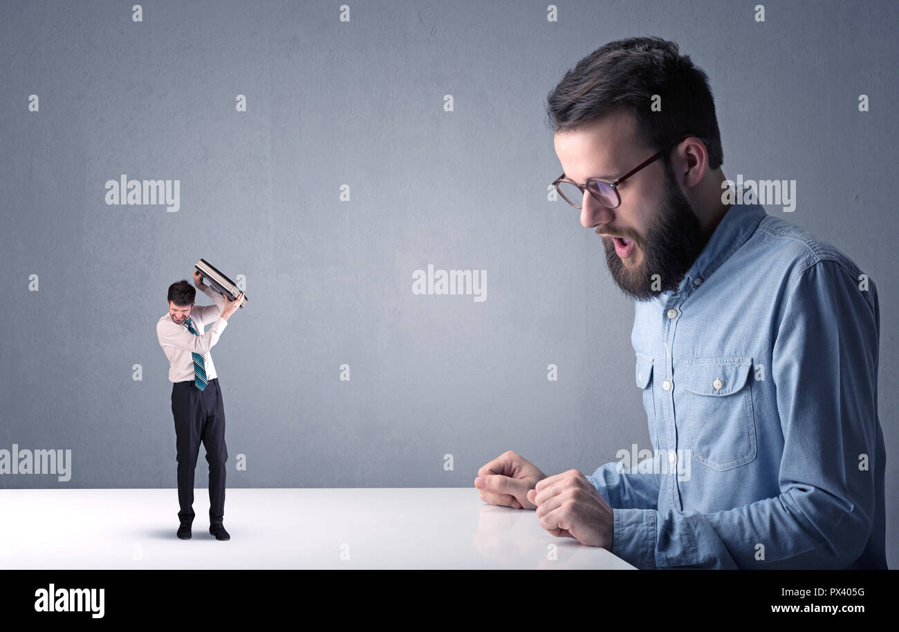 Giovane imprenditore professionale essendo arrabbiato con un altro imprenditore in miniatura nella parte anteriore di un bluastro sfondo grigio Foto Stock