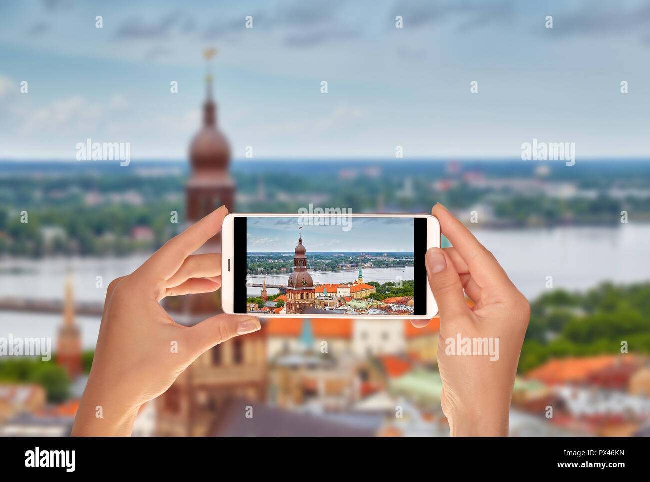 Un turista è scattare una foto della vista della città di Riga da sopra, inclusi la Torre della cattedrale del Duomo su un telefono cellulare Foto Stock