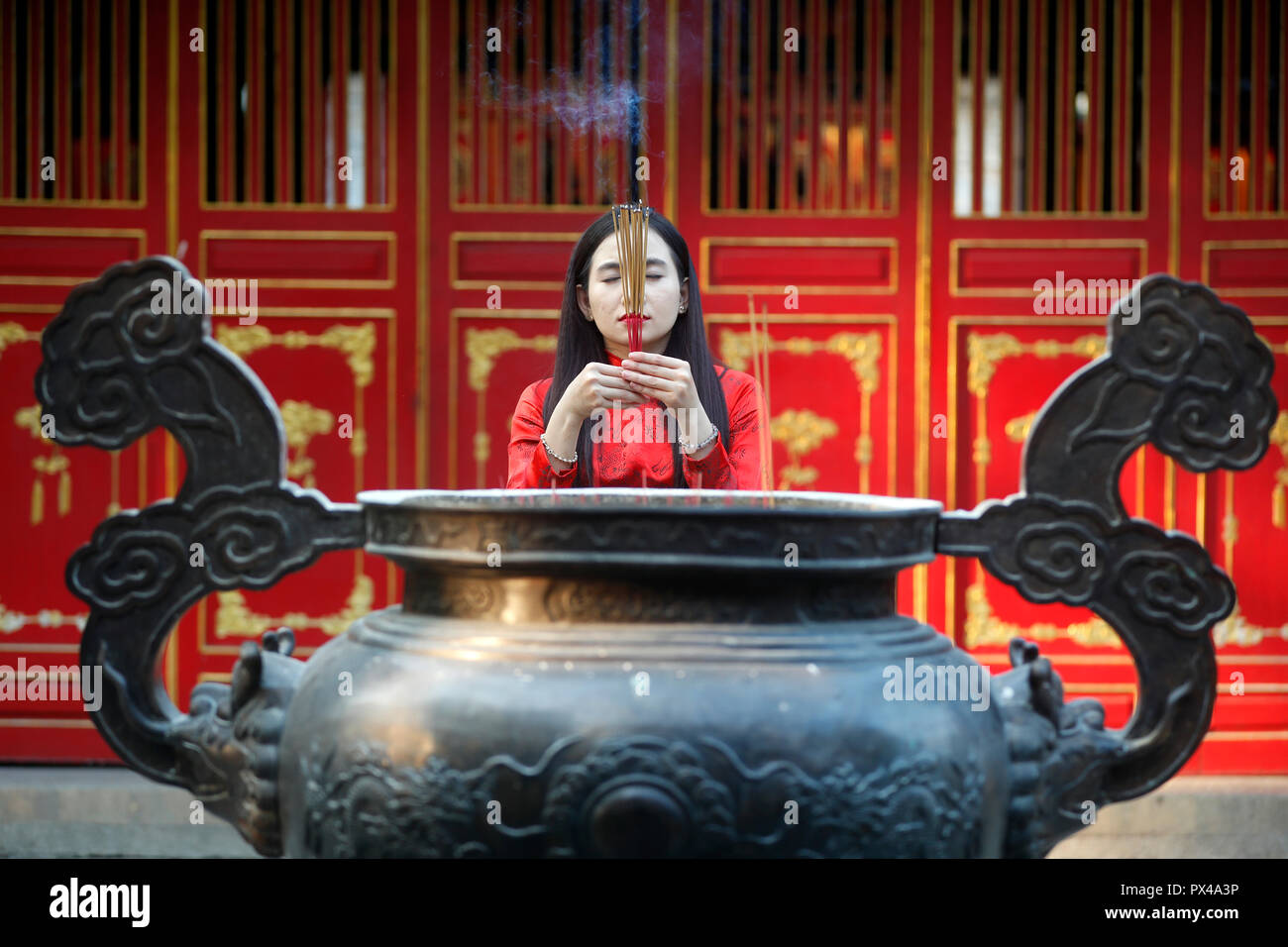 Donna vietnamita in rosso tradizionale abito lungo Ao Dai pregando con bastoncini di incenso. Ho Chi Minh City. Il Vietnam. Foto Stock