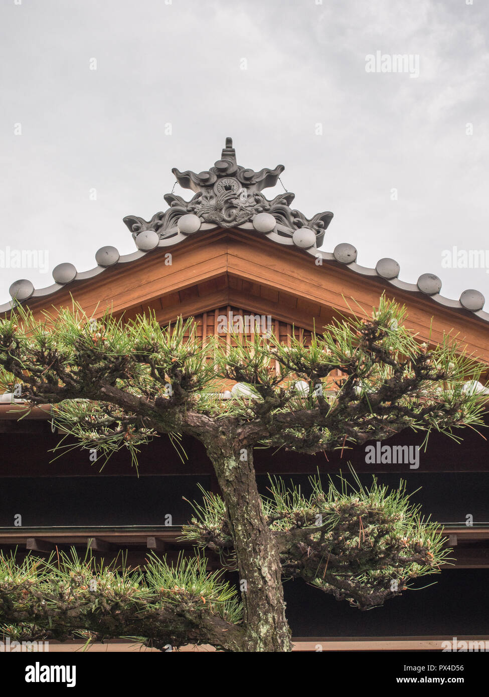 Timpano del tetto con tradizionale kawara piastrelle decorative, cloud e potatura di alberi di pino, Shikoku-Chuo, Ehime Giappone Foto Stock