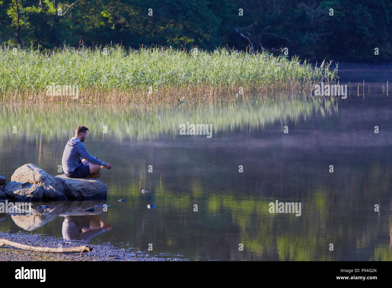 Un uomo sul suo proprio seduto su una roccia sul bordo di un lago Foto Stock
