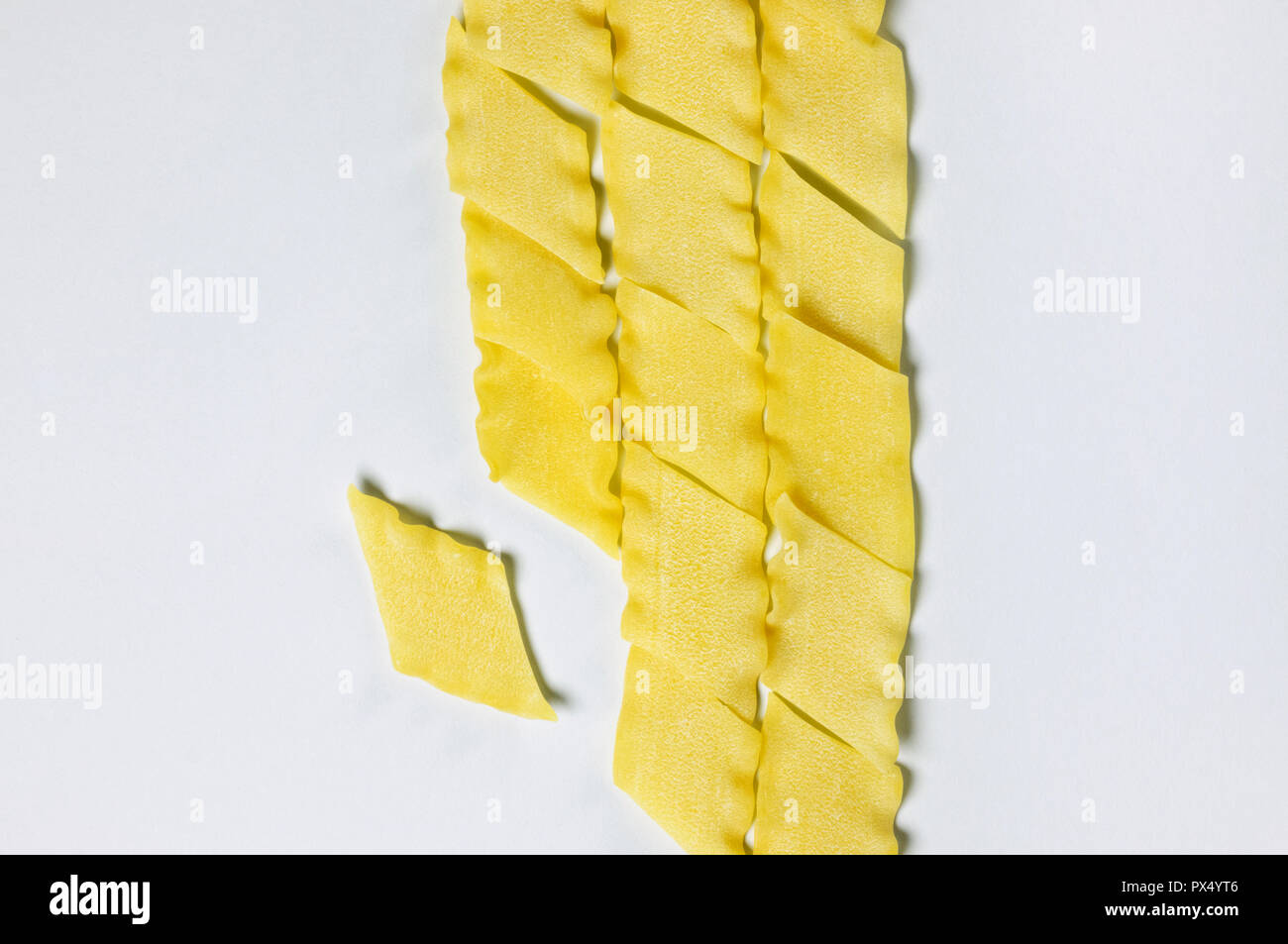 Asciugare la pasta italiana chiamato pantacce su uno sfondo bianco ,rhombus -pasta sagomata con bordo ondulato ,divertente composizione , studio shot , vista superiore Foto Stock