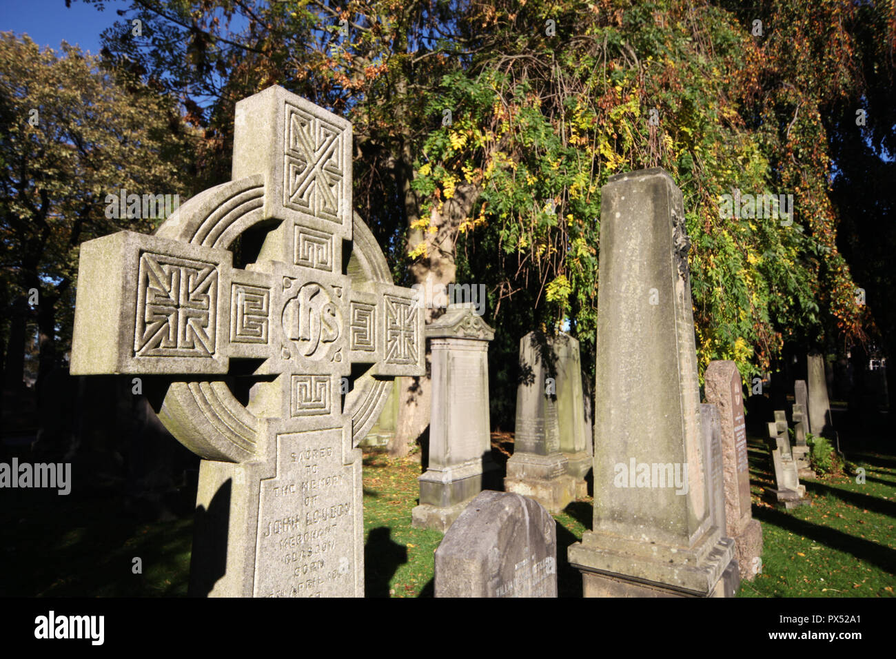 Il pomeriggio di sole illumina alcune delle lapidi con gli alberi in background cominciando a mostrare segni di un cambiamento autunnali nel cimitero di Dean Foto Stock