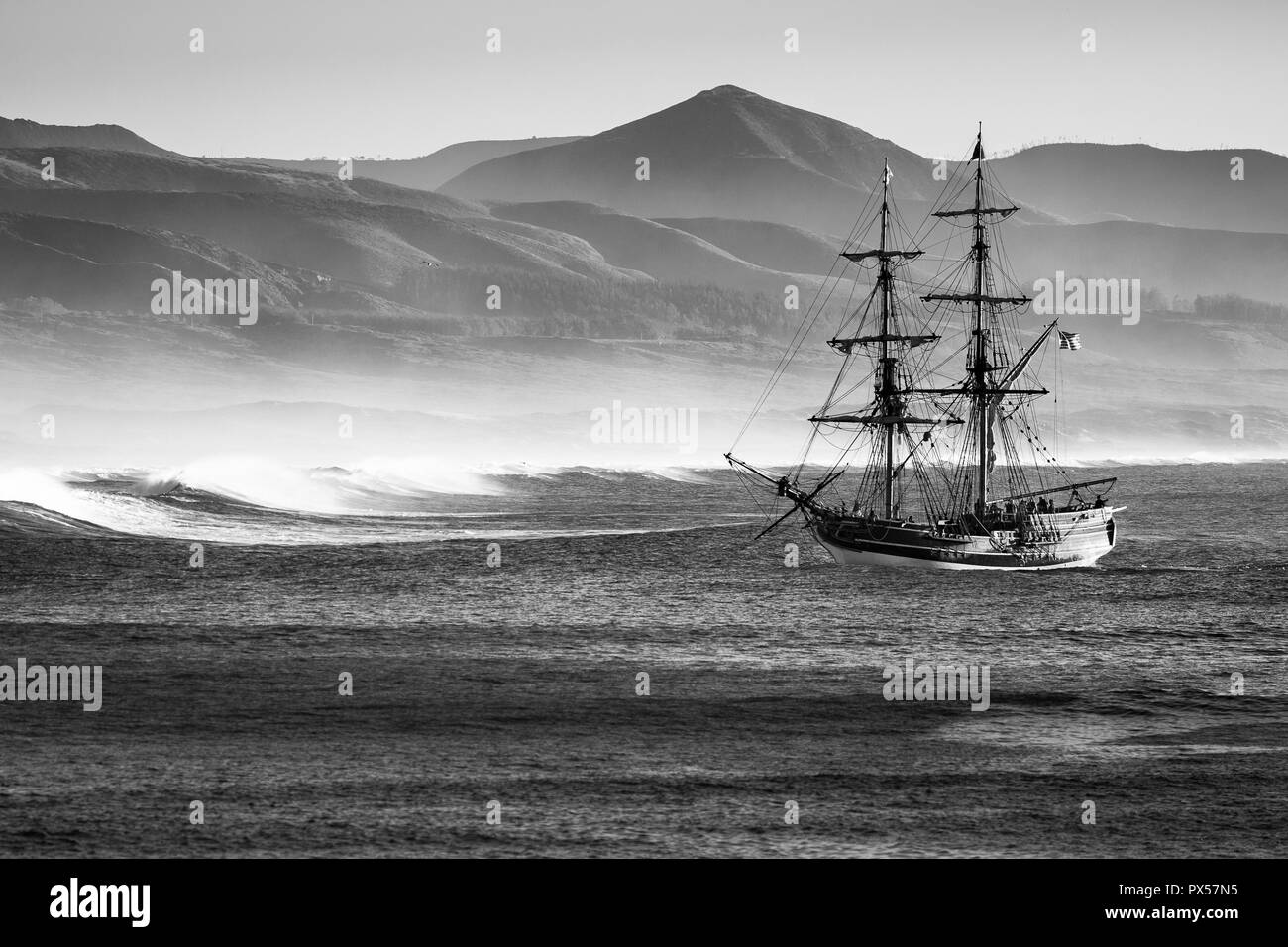 Tradizionale due-masted veliero giunge a Morro Bay Harbour per il rigonfiamento dell'Oceano Pacifico. Surf e tardo pomeriggio decrescente di nebbia sulle colline b Foto Stock