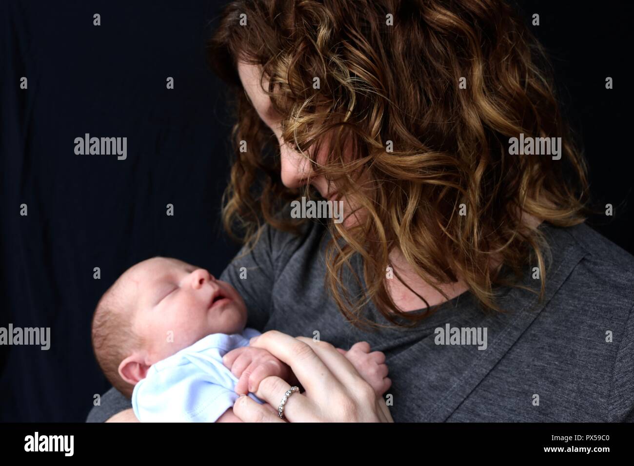 Madre teneramente guardando il neonato contro uno sfondo nero Foto Stock