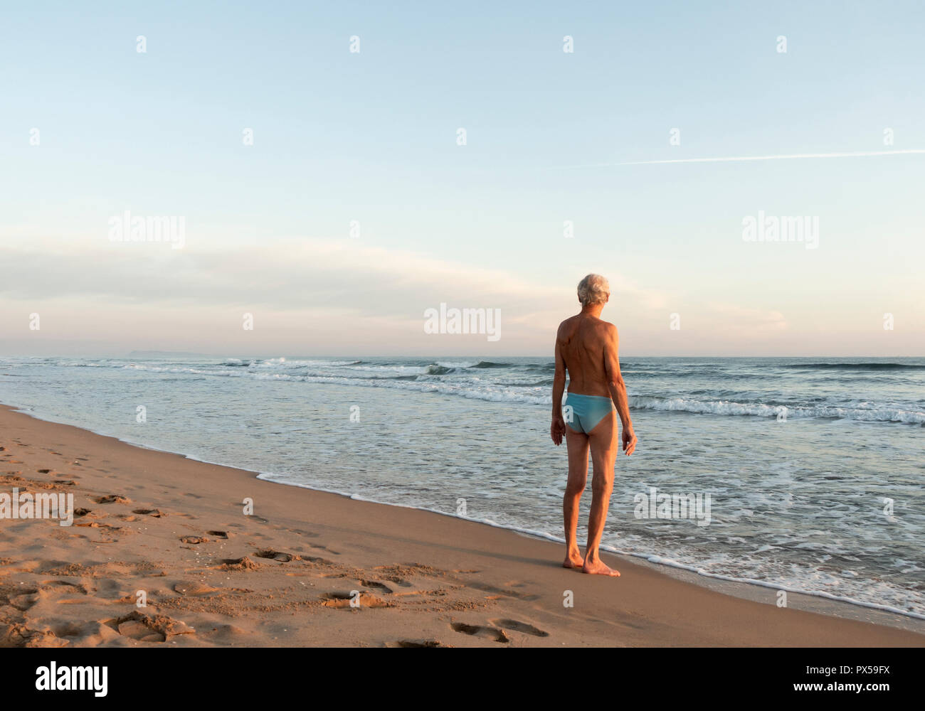 Uomo anziano stretching prima di nuotare sulla spiaggia a sunrise. Foto Stock