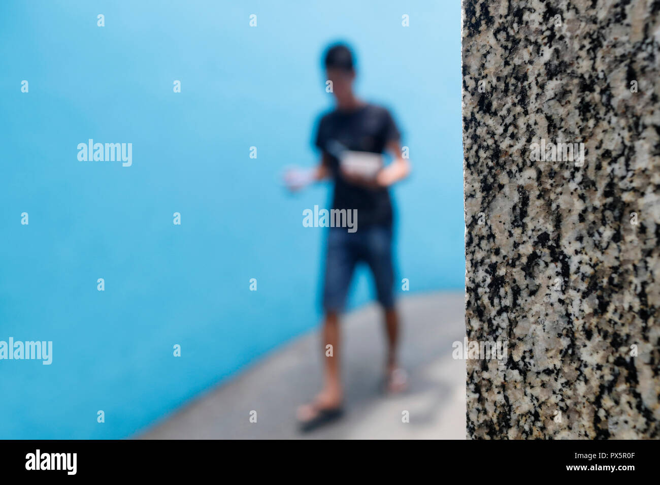 Ragazzo a piedi su una piccola strada contro un muro di blu. Uomo che cammina su una piccola strada contro un muro di blu. Ho Chi Minh City. Il Vietnam. Foto Stock