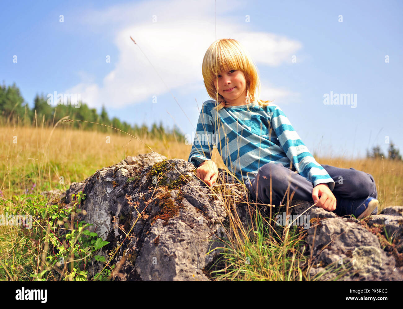 Ritratto di un ragazzo seduto sulla grande pietra all'aperto Foto Stock