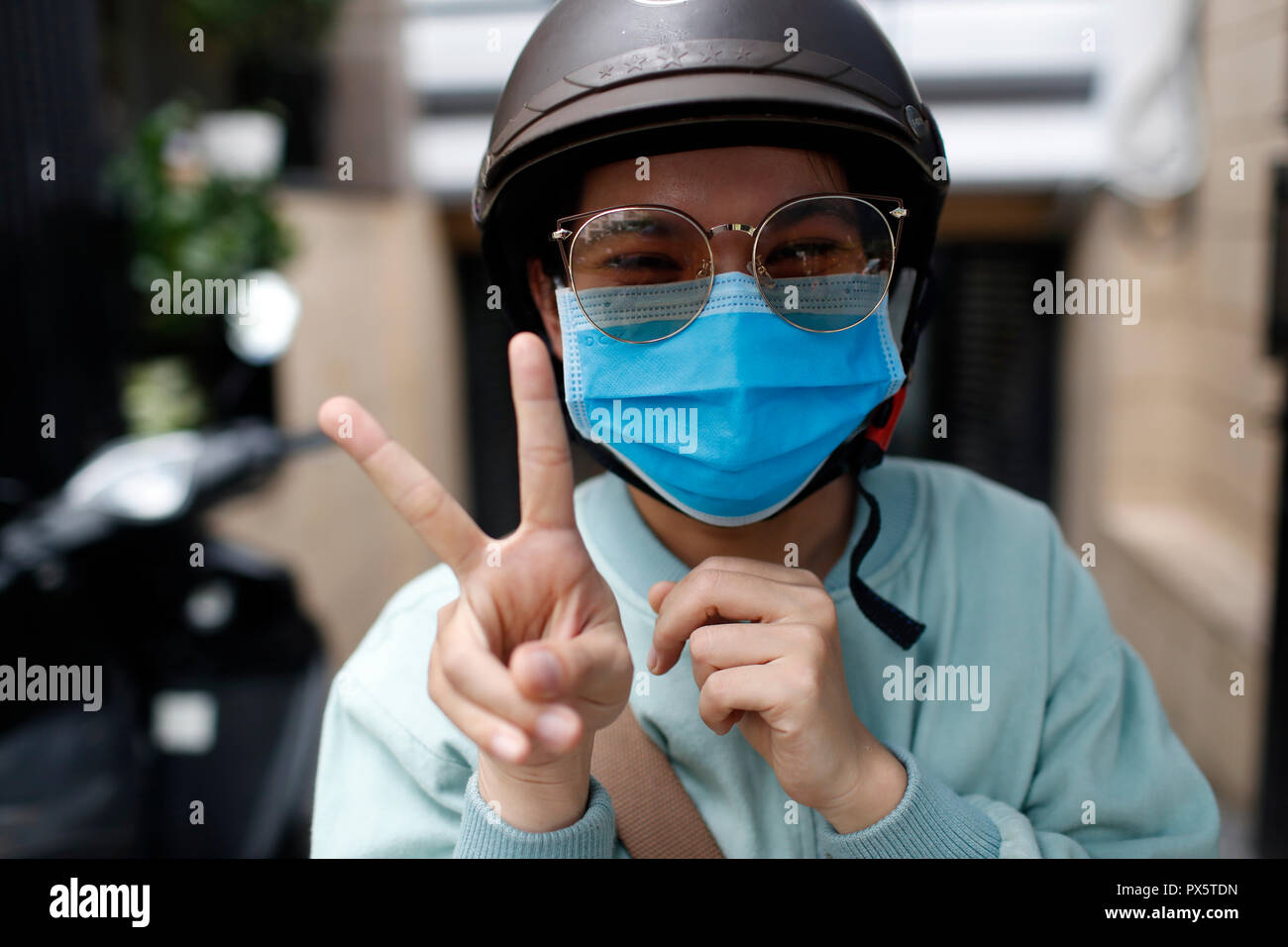 Ragazza vietnamita con il casco e la maschera. Segno di vittoria. Ritratto. Ho Chi Minh City. Il Vietnam. Foto Stock