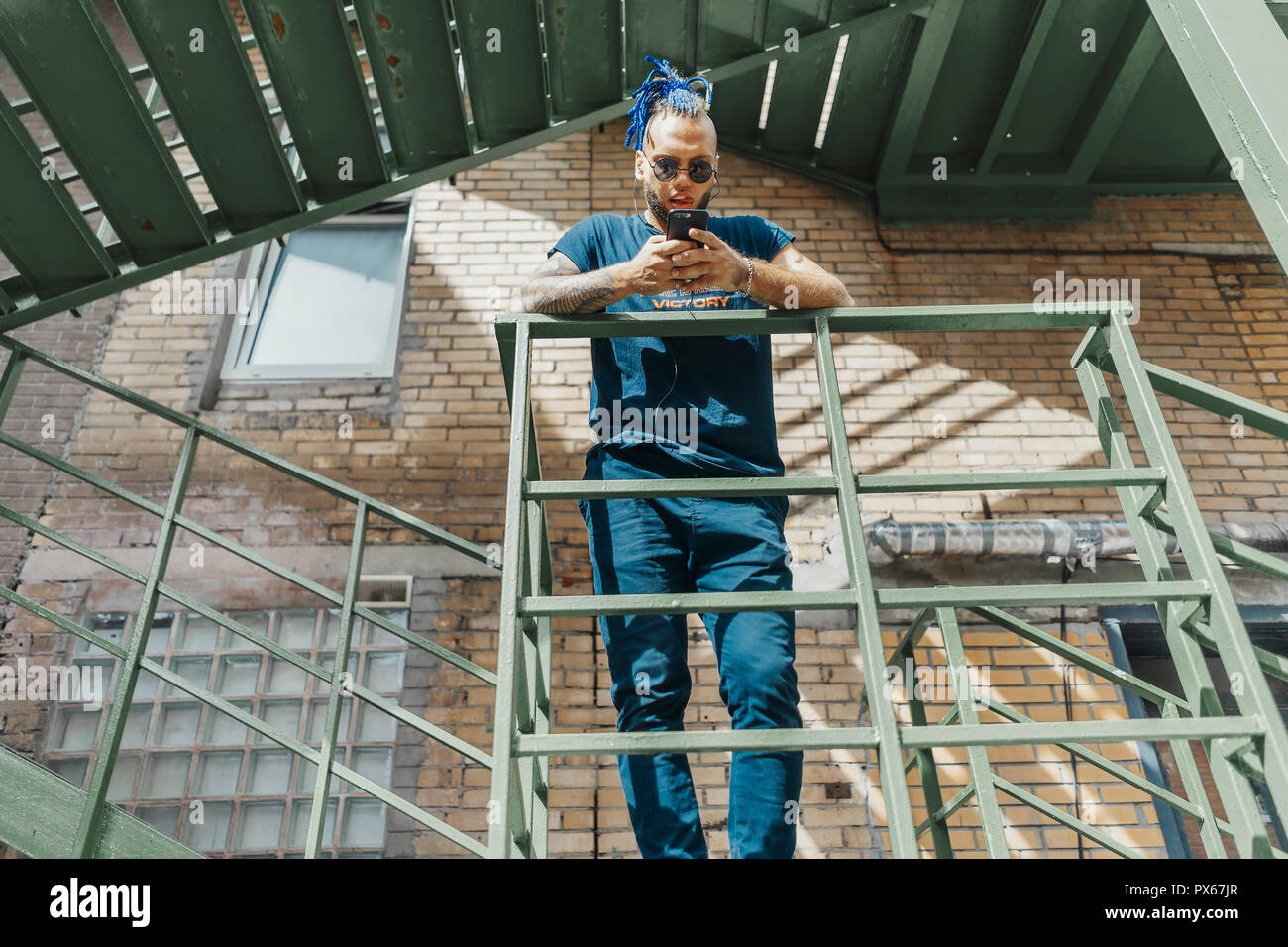 Giovane uomo attraente con blue dreadlocks in piedi alla scala. Foto Stock