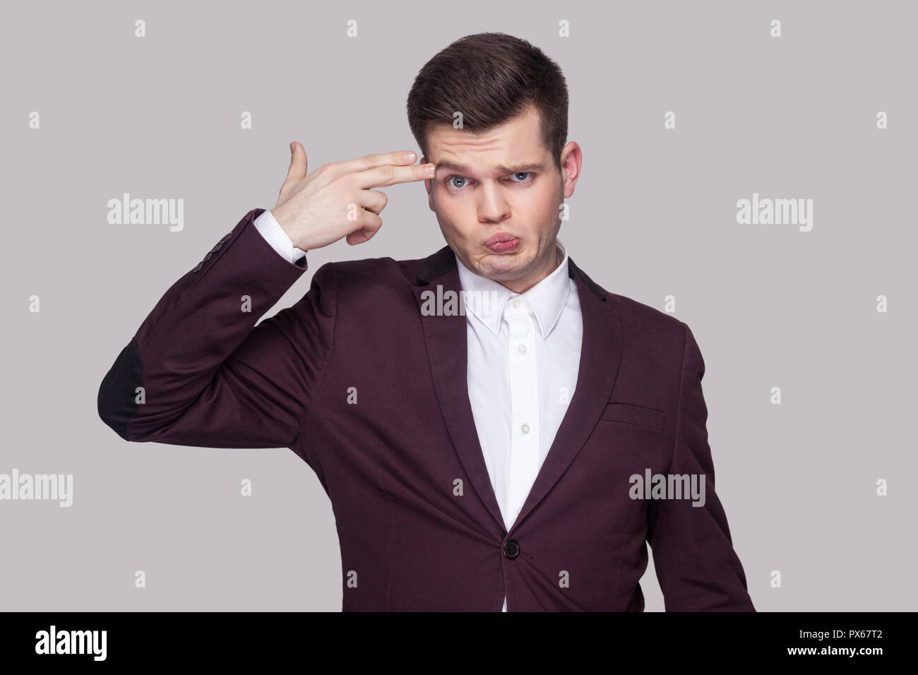 Ritratto di confuso bel giovane in tuta viola e una camicia bianca, in piedi, guardando la telecamera con faccia grave e gesto di pistola. piscina studio s Foto Stock