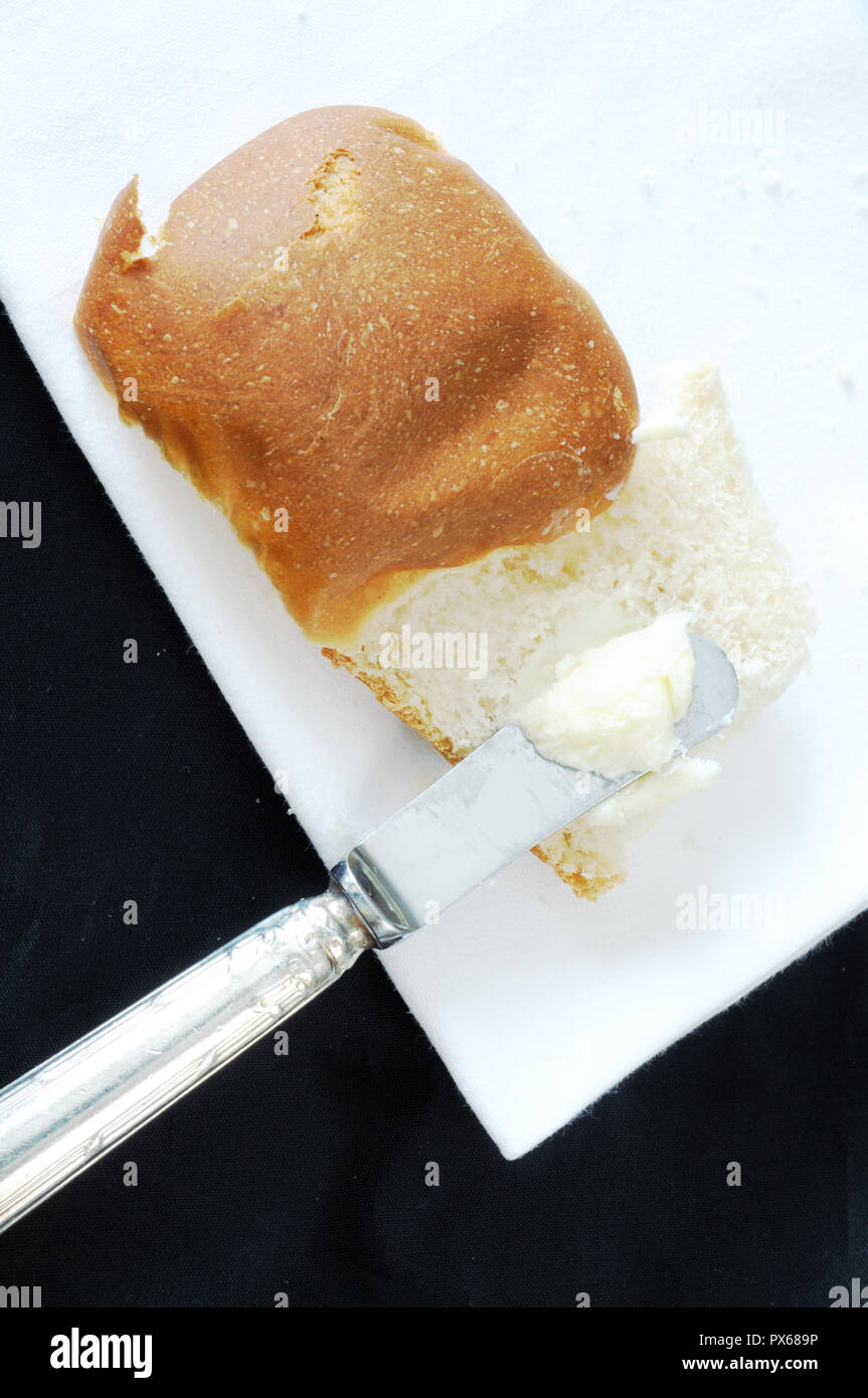 Vista dall'alto di un ricciolo di burro spalmato su un panino, su sfondo nero, verticale Foto Stock