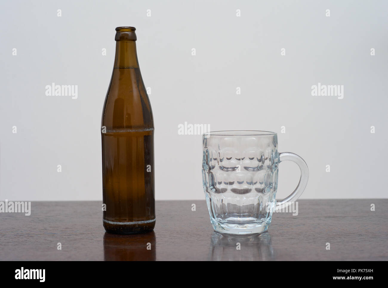 Svuotare il bicchiere con pinta di vetro e una bottiglia di birra Una tavola di legno marrone Foto Stock