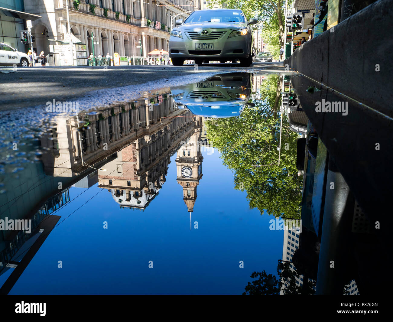Un momento nel tempo catturati come riflessi di edifici della città e più persone di andare circa la loro vita sono visto in una visione distorta in una pozza Foto Stock
