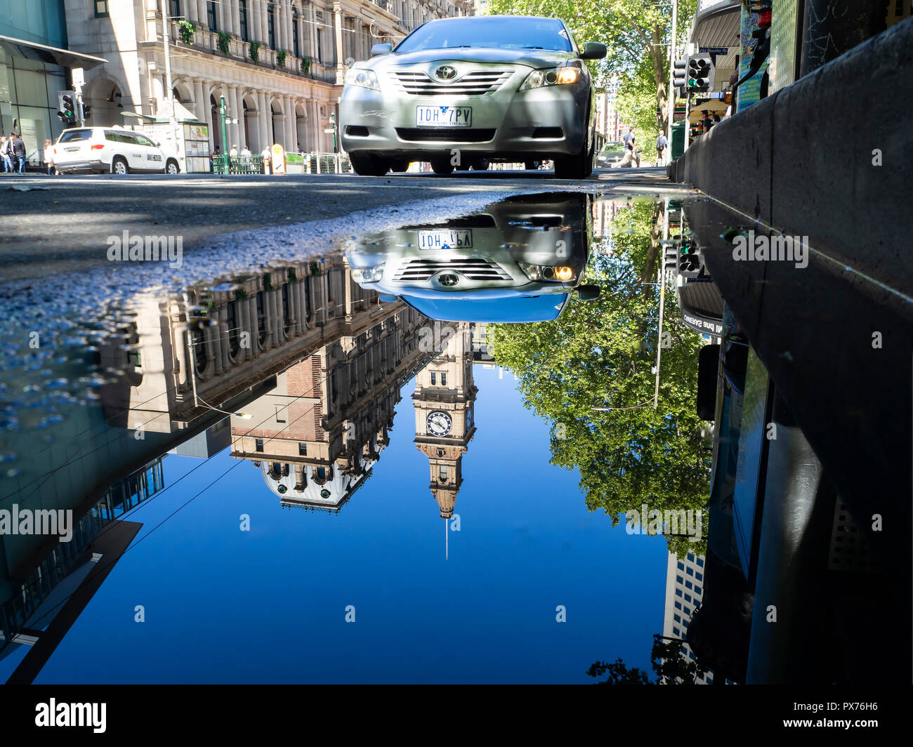 Un momento nel tempo catturati come riflessi di edifici della città e più persone di andare circa la loro vita sono visto in una visione distorta in una pozza Foto Stock
