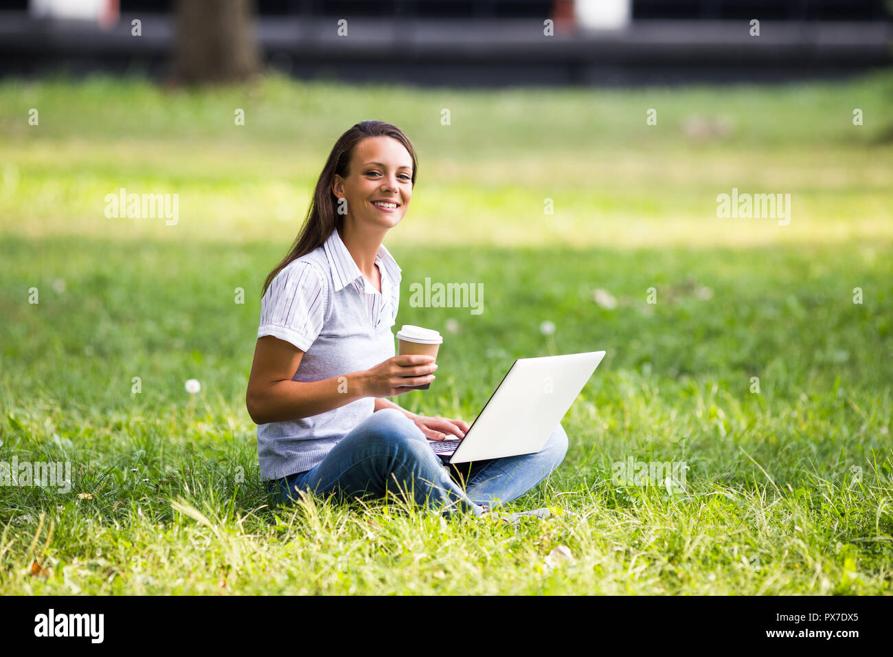 Bella imprenditrice è a bere caffè e utilizzando computer portatile durante il riposo dal lavoro al parco. Foto Stock