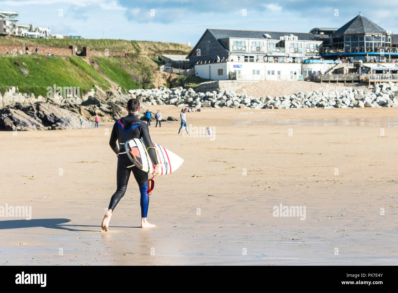 Un surfista portando la sua tavola da surf a piedi su Fistral Beach in Newquay in Cornovaglia. Foto Stock